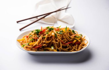 Schezwan erişte veya sebze Hakka erişte veya chow mein tahta çubukla bir kase veya plaka servis popüler Hint-Çin yemek tarifleri, var. seçici odak