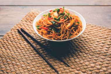 Schezwan erişte veya sebze Hakka erişte veya chow mein tahta çubukla bir kase veya plaka servis popüler Hint-Çin yemek tarifleri, var. seçici odak