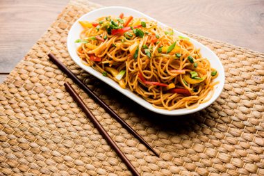 Schezwan erişte veya sebze Hakka erişte veya chow mein tahta çubukla bir kase veya plaka servis popüler Hint-Çin yemek tarifleri, var. seçici odak