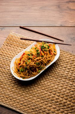 Schezwan erişte veya sebze Hakka erişte veya chow mein tahta çubukla bir kase veya plaka servis popüler Hint-Çin yemek tarifleri, var. seçici odak