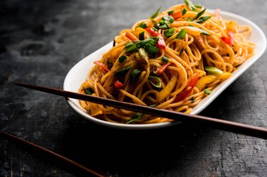 Schezwan erişte veya sebze Hakka erişte veya chow mein tahta çubukla bir kase veya plaka servis popüler Hint-Çin yemek tarifleri, var. seçici odak