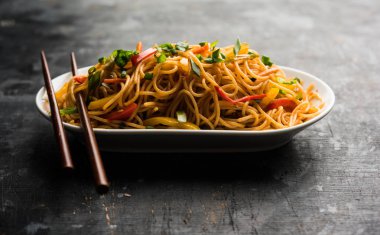 Schezwan erişte veya sebze Hakka erişte veya chow mein tahta çubukla bir kase veya plaka servis popüler Hint-Çin yemek tarifleri, var. seçici odak