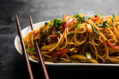 Schezwan erişte veya sebze Hakka erişte veya chow mein tahta çubukla bir kase veya plaka servis popüler Hint-Çin yemek tarifleri, var. seçici odak