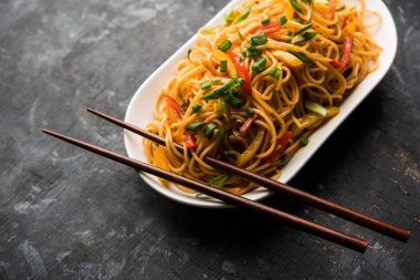 Schezwan erişte veya sebze Hakka erişte veya chow mein tahta çubukla bir kase veya plaka servis popüler Hint-Çin yemek tarifleri, var. seçici odak