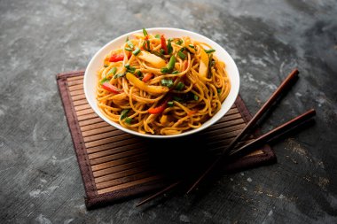 Schezwan erişte veya sebze Hakka erişte veya chow mein tahta çubukla bir kase veya plaka servis popüler Hint-Çin yemek tarifleri, var. seçici odak