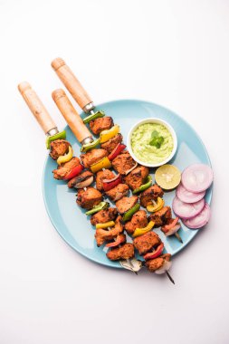 ızgara tavuk tikka şiş üzerinde. bir tabak yeşil Hint turşusu ve soğan ile servis. Seçici odak