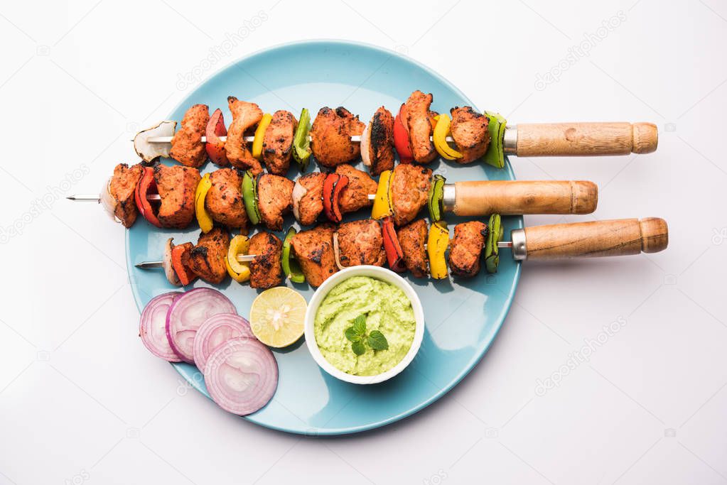 grilled chicken tikka on skewers.  served in a plate with green chutney and onion. Selective focus