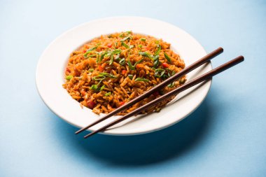 Schezwan Fried Rice Masala is a popular indo-chinese food served in a plate or bowl with chopsticks. selective focus clipart