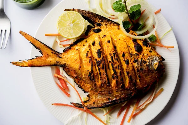 Tandoori Pomfret fish cooked in a clay oven and garnished with lemon , mint, cabbage and carrot salad. Selective focus