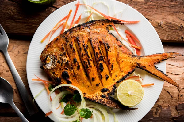 Tandoori Pomfret fish cooked in a clay oven and garnished with lemon , mint, cabbage and carrot salad. Selective focus