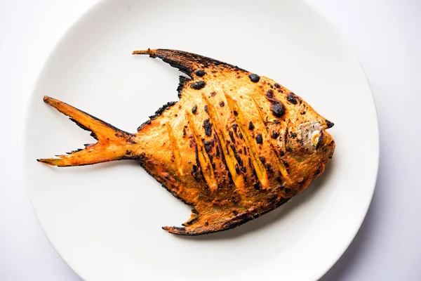 Tandoori Pomfret fish cooked in a clay oven and garnished with lemon , mint, cabbage and carrot salad. Selective focus