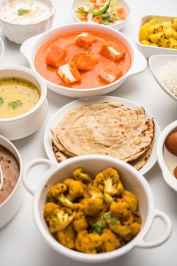 Paneer tereyağı masala, dal makhani, roti, pirinç, sabji, gulab jamun ve bağlı raita gibi çeşitli Hint gıda karamsar arka plan, seçici odak üzerinde kaselerde servis