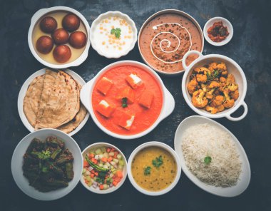 Paneer tereyağı masala, dal makhani, roti, pirinç, sabji, gulab jamun ve bağlı raita gibi çeşitli Hint gıda karamsar arka plan, seçici odak üzerinde kaselerde servis