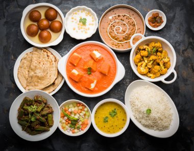 Paneer tereyağı masala, dal makhani, roti, pirinç, sabji, gulab jamun ve bağlı raita gibi çeşitli Hint gıda karamsar arka plan, seçici odak üzerinde kaselerde servis