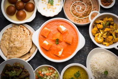 Paneer tereyağı masala, dal makhani, roti, pirinç, sabji, gulab jamun ve bağlı raita gibi çeşitli Hint gıda karamsar arka plan, seçici odak üzerinde kaselerde servis