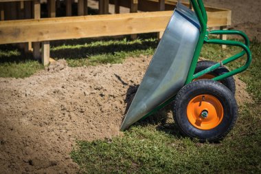 Boş bir el arabası boş kum, inşaat ve teçhizatın yanında duruyor.