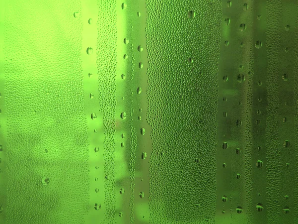 Green misted glass with drops of water, abstract background with uneven lighting