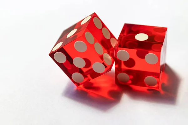 Two red glass dice on a gray background in sunlight. Result 1 and one on the edge, close-up with selective focus.