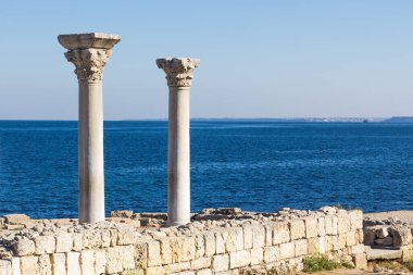 Two columns from the excavations of the ancient basilica in Chersonese against the background of the sea clipart