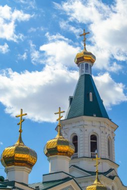 Rusya 'nın Omsk kentindeki Ortodoks kilisesinin çan kulesi ve kubbeleri bulutlu mavi gökyüzüne karşı..
