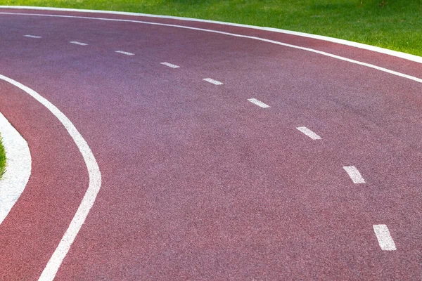 Red synthetic treadmill or cycle track with white markings, turns to the left