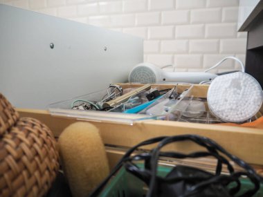 Kozmetik, pamuk tomurcukları ve saç kurutma makinesi ile dağınık açık banyo çekmecesi