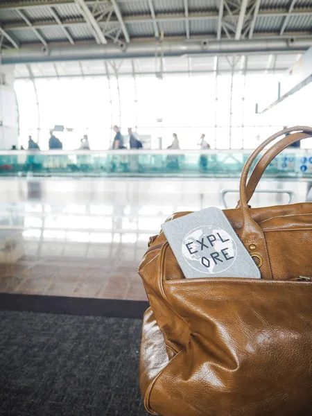 Bag and passport cover with motivational quote \'Explore\' in a airport terminal with travelers in the background