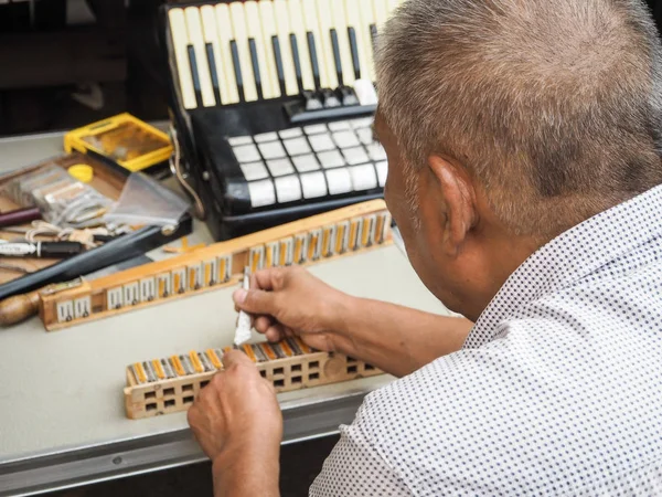 Old man repairing the reed blocks of a vintage accordion, Beijing, China