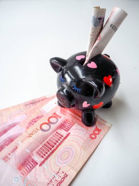 Black piggy bank standing next to Chinese 100 rmb banknotes on a white wooden background. The pig symbols fortune in the Chinese zodiac.