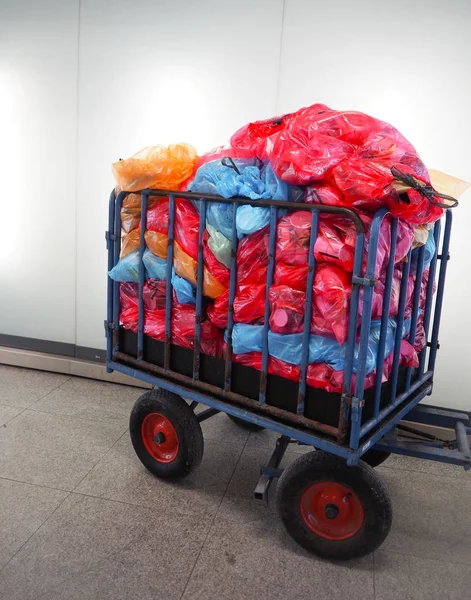 Metal cart for waste collection with a large pile of colorful plastic bags filled with sorted waste ready for disposal