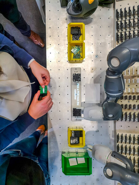 Caucasian female operator standing at an assembly workstation with a collaborative robot
