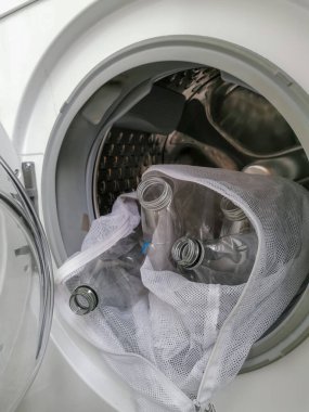 Çamaşırhane sırasındaki mikro plastik atığı temsil eden plastik şişelerle dolu çamaşır makinesi.