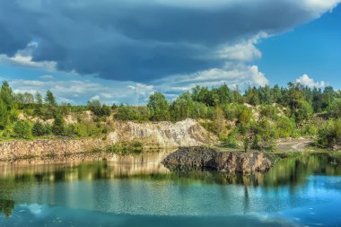 Bazalt göl güneşli gün. Shore, kayalar, mavi gökyüzü bulutlu onlar üzerinde orman.