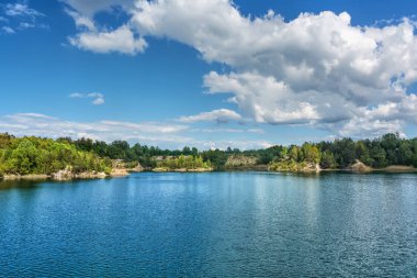 Bazalt göl güneşli gün. Shore, kayalar, mavi gökyüzü bulutlu onlar üzerinde orman.
