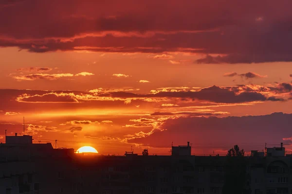 The sun and sky with clouds over silhouettes of city roofs at sunset.