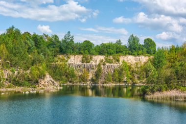 Bazalt göl güneşli gün. Shore, kayalar, mavi gökyüzü bulutlu onlar üzerinde orman.