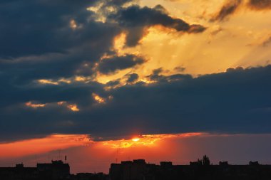Güneş, gökyüzü bulutlu gün batımında akşam şehrin siluetleri üzerinde.