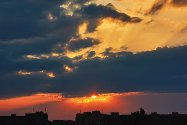 Sun, sky with clouds over silhouettes of the evening city at sunset.