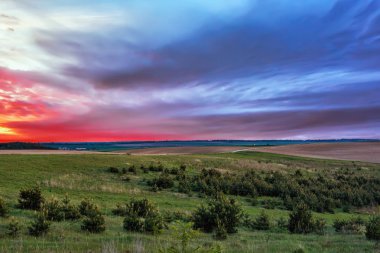 Gökyüzü bulutlu meadows, alanları ve ormanları üzerinde günbatımında.
