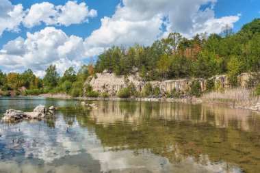Bazalt göl güneşli gün. Shore, kayalar, mavi gökyüzü bulutlu onlar üzerinde orman.