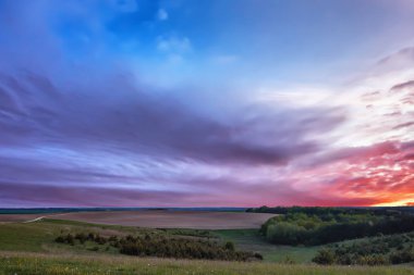 Çayır, sürülmüş alan ve orman güzel bulutlu gün batımında.