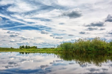 Üstündeki bulutlar ile nehir banka, mavi gökyüzü güneşli gün.