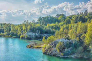 Bazalt göl güneşli gün. Shore, kayalar, mavi gökyüzü bulutlu onlar üzerinde orman.