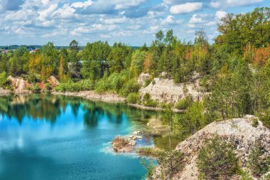 Bazalt göl güneşli gün. Shore, kayalar, mavi gökyüzü bulutlu onlar üzerinde orman.