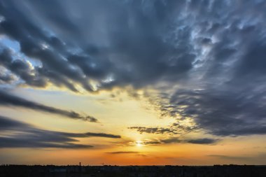 Güneş, gökyüzü bulutlu gün batımında şehir üzerinde.