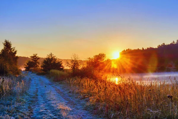 Sunrise over the shore of the lake, a dirt road covered with frost.