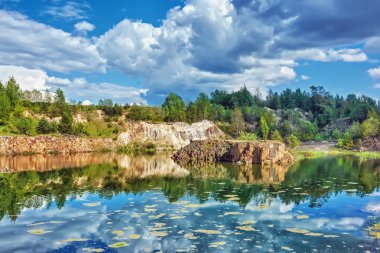 Bazalt göl güneşli gün. Shore, kayalar, mavi gökyüzü bulutlu onlar üzerinde orman.