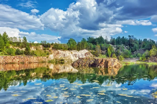 Bazalt göl güneşli gün. Shore, kayalar, mavi gökyüzü bulutlu onlar üzerinde orman.