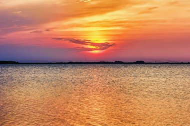 Gün batımı göl üzerinde ters banka siluetleri ki, gökyüzü bulutlu su yansıtılır.