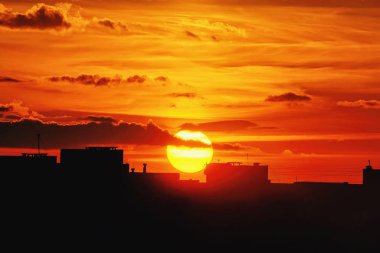 Manzara - güneş batımında bulutlu, çatıları siluetleri ön plan.